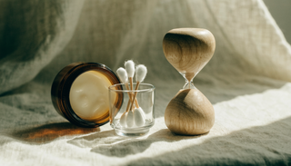 A small amber jar, cotton buds and an hourglass on cream linen