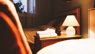 A calm bedside at dusk with folded cotton pyjamas and a small amber jar