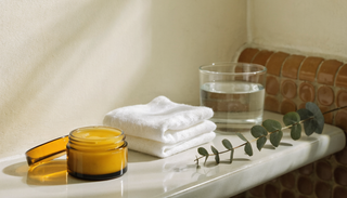 Open jar of golden balm with a cotton flannel on a calm bathroom shelf
