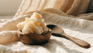 Raw shea butter chunks in a wooden bowl on cream linen