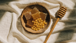 Honeycomb and beeswax pellets in a wooden bowl on cream linen