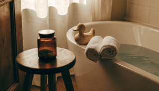 Rolled towels and a wooden toy duck beside a small amber jar at bath time