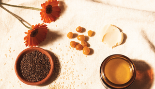 Natural balm ingredients laid out on linen: calendula, seeds, beeswax and shea butter